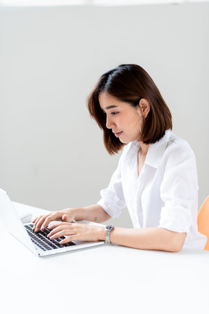 Young happy Asian woman working in a white office with laptop.の写真素材