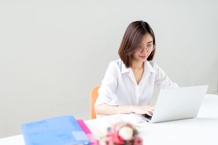 Young happy Asian woman working in a white office with laptop.