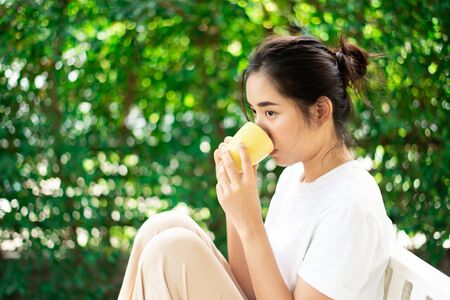 Selective focus at young Asian Thai woman drink a coffee in home garden with green plant background.の写真素材