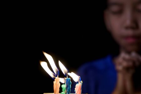 Young Asian boy celebrate and blow the candle of his birthday cake in a dark room.