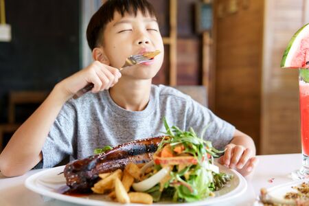 Young Asian boy eat fried port and salad in a resturant.の写真素材