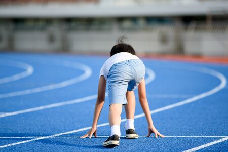 Young Asian boy prepare to start to run on a blue track in summer day