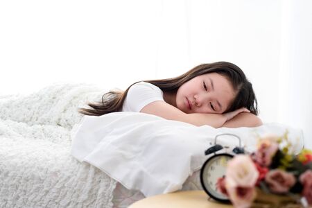 Selective focus at sleeping girl on a white bed beside an alarm clock.の写真素材
