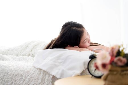 Selective focus at sleeping girl on a white bed beside an alarm clock.