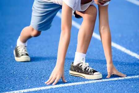 Young Asian boy prepare to start run on a blue track in summer dayの写真素材