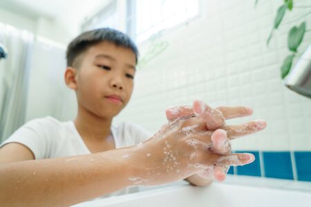 Selective focus at hand of young Asian boy washing with faucet in a bathroom.の写真素材