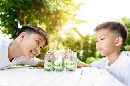 Selective focus at coin from a young asian Thai boy putting in a glass bottle in a garden. Money and saving concept.の写真素材