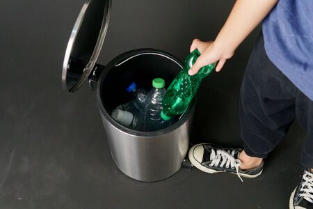 Child hand drop a plastic waste and bottle in a trash bin.