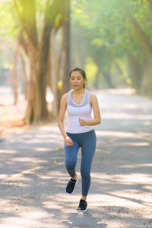 Selective focus at young Asian woman running with happy in a park during summer day in a morning.の写真素材