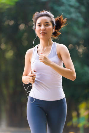 Selective focus at young Asian woman running with happy in a park during summer day in a morning.の写真素材