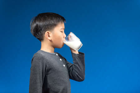 Young Asian boy drink milk from a glass on blue background