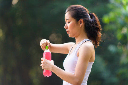 Close up young Asian woman drink water from a plastic bottle after do sport in the morning in a park during summer dayの写真素材