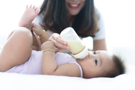 Close up mom feeding milk from a bottle to baby in a bedroomの写真素材