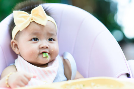 Female Baby eating soft food from tray on high chare in a gardenの写真素材