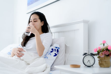 Young Asian woman drink water from a glass after wake up in the morning in a bedroom.の写真素材