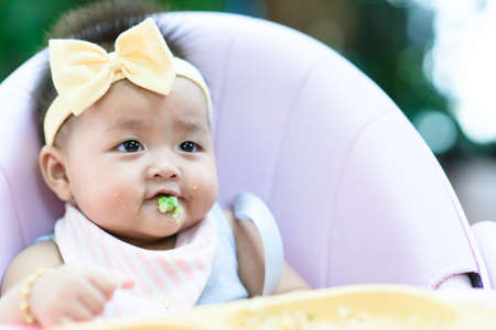 Female Baby eating soft food from tray on high chare in a gardenの写真素材