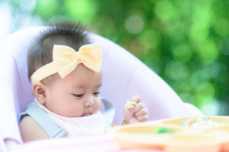 Female Baby eating soft food from tray on high chare in a gardenの写真素材
