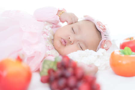 Portrait sleeping Asian female baby with variety of fruits on white bedの写真素材
