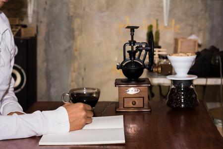 Woman writing a notepad on a wooden desk at a coffee shop.