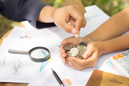 A hand adding a coin in a handful of coins. Money saving ideasの写真素材