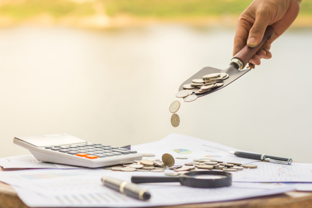A male hand putting a scoop of coins on a pile, saving money concept,の写真素材