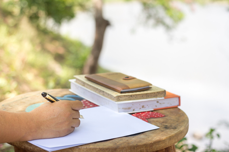 Man's hand with pen writing on notebook in parkの写真素材