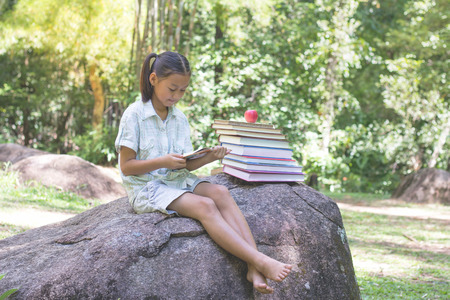 A girl sitting on a rock reading a book.,natural background,educational and Scientific Conceptsの写真素材