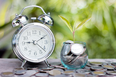 Close up of time and money with green bokeh background, Save money for prepare in the future.の写真素材