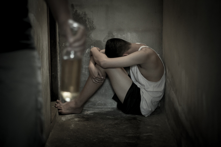 The child sits in the corner of the room, fearing the drunken man will hurt., Stop violence in children Help prevent abuse and bring him back to family ,Fathers alcoholism.の写真素材