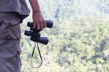 Young male hiker hand holding binoculars  relaxing on top of a mountain- Holiday activities. - Pictures with space for editing.の写真素材