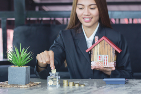 Human hands insert coin in a glass jar and  holding house figure in another , Savings money jar full of coins concept for saving or investment for a house.の写真素材