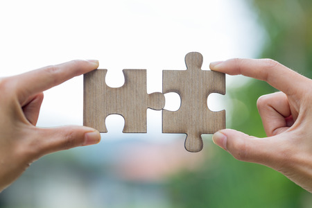 Two hands trying to connect couple puzzle piece with green background.  symbol of association and...