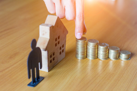 Hand putting money coin stack with wooden house; Property investment and house mortgage financial concept,の写真素材