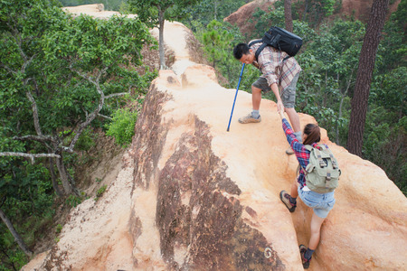 Team of climbers man and woman help each other on top of mountain, climbing hiking together, Young tourists with backpacks,の写真素材