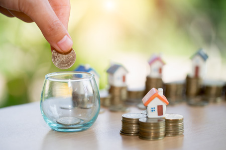 A men hand holding stacking gold coins and house model, saving money for buying a new home and investment with real estate concept.の写真素材
