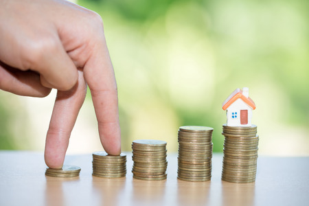 Close up of hand with climb up on a stacking gold coins and home as destinations, Loans for real estate or buy a new house.の写真素材