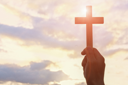 Silhouette off hands holding wooden cross  on sunrise background, Crucifix, Symbol of Faith.