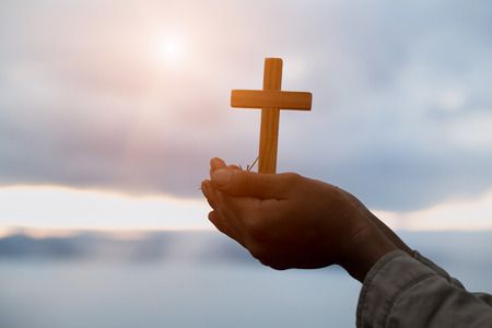 Silhouette off hands holding wooden cross  on sunrise background, Crucifix, Symbol of Faith.の写真素材