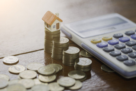 House model on coins stacks with calculator as background. Concept for property ladder, mortgage and real estate investment.の写真素材