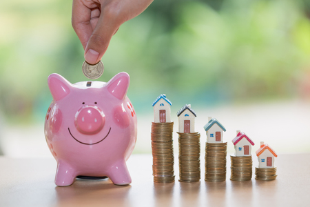 Hand putting coin into  piggy bank, Saving money to buy a home, Real estate or home savings, piggy bank, coins and a house,の写真素材