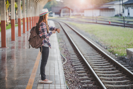 Beautiful young asian woman traveler looking clock  with brown bag ,Waiting for train at train station, Chinese tourists, Travel and vacation concept.の写真素材