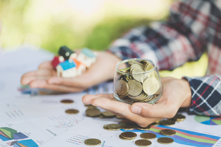 Investor show hand holding a model home and coin , Saving money for buy a new house and loan for plan business investment for real estate in the future concept, Invesment and Risk Management.の写真素材
