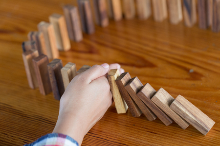 Businessman hand stopping falling wooden dominoes effect from continuous toppled or risk, strategy and successful intervention concept for business, game strategy, Invesment and Risk Management.の写真素材