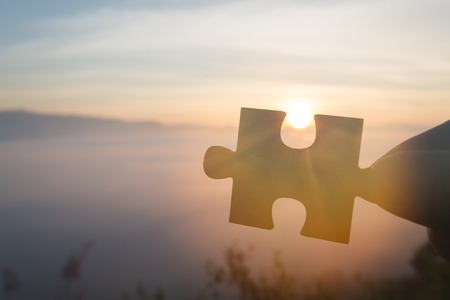 Silhouette of hand holding Jigsaw with Sunrise background. . symbol of association and connection. business strategy.の写真素材