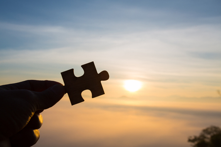 Silhouette of hand holding Jigsaw with Sunrise background. . symbol of association and connection. business strategy.の写真素材