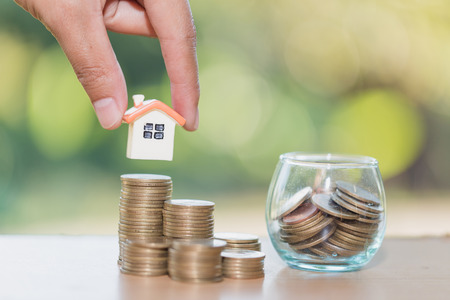Woman hand hold a  home model put on the stack coin with growing, Savings money for buy house and loan to business investment for real estate concept. Invesment and Risk Management.の写真素材