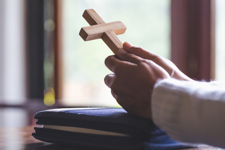 Hands folded in prayer on a Holy Bible  in church concept for faith, spirtuality and religion, Human hand holds cross, Worship, sins and prayer.の写真素材