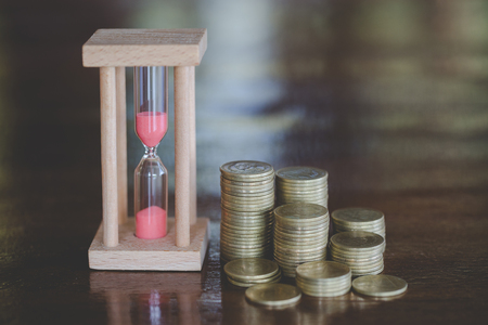 Hourglass with coins on wooden  background, Time investment and retirement saving. Urgency countdown timer for business deadline concept.の写真素材