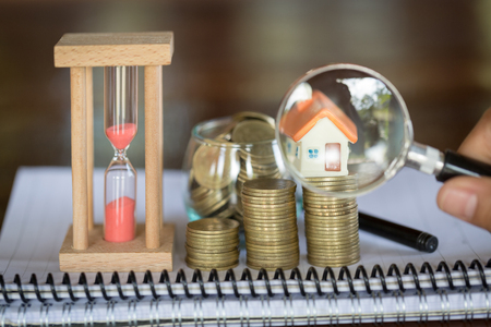 Stack coin and bar graph with grow,  Hand hold a magnifying glass searching for a new home, Loan for real estate or save money for buy a house to family in the future concept.の写真素材