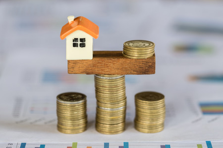 Model house and money coins balancing on a seesaw, Property real estate investment ideas, Concept of risk house mortgage, loan financial management.の写真素材
